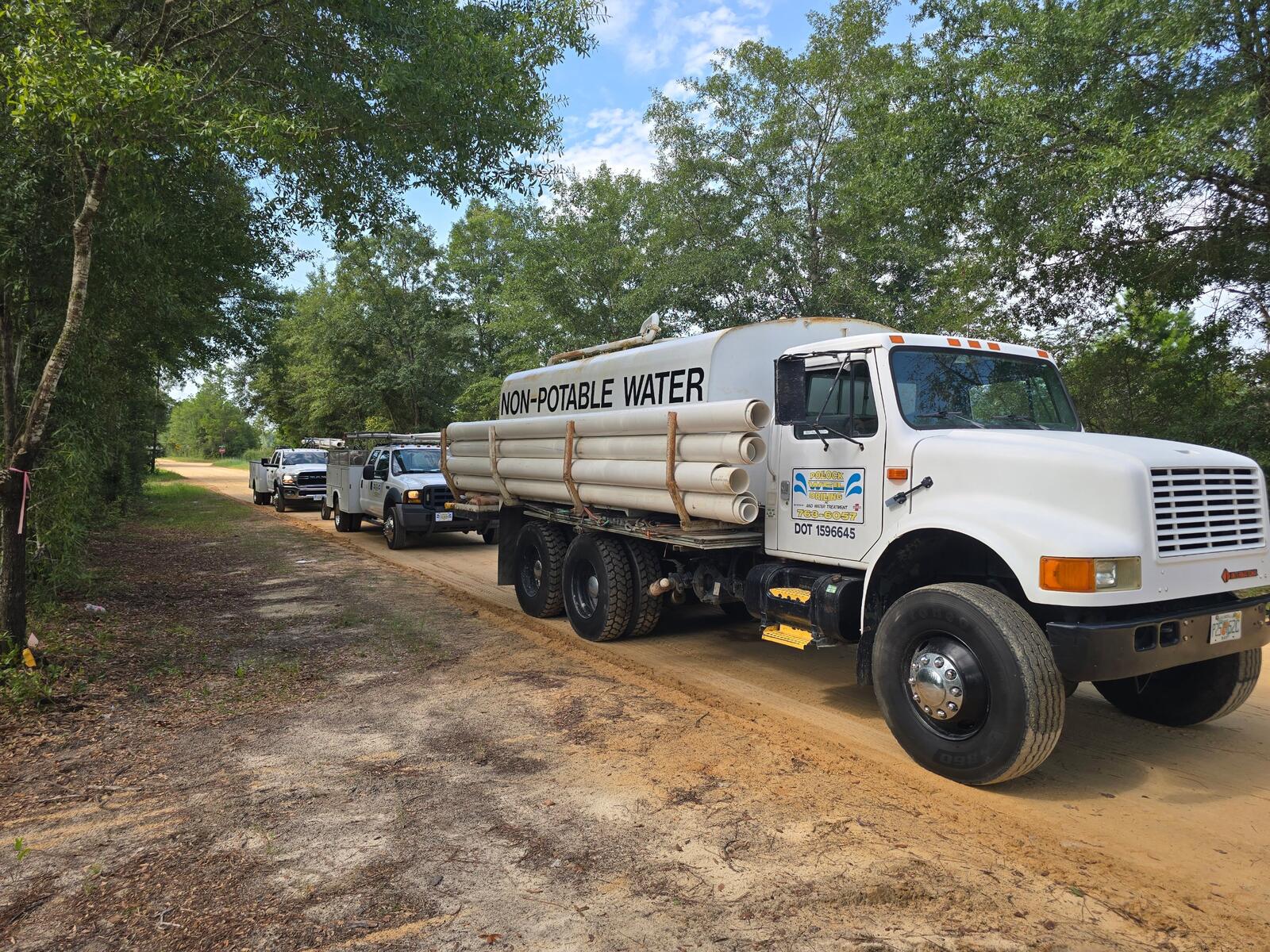 Pollock non-potable water truck carrying PVC well casing, followed by service trucks
